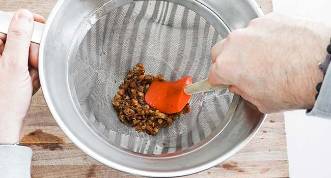 pressing down pork cracklings through a chinois