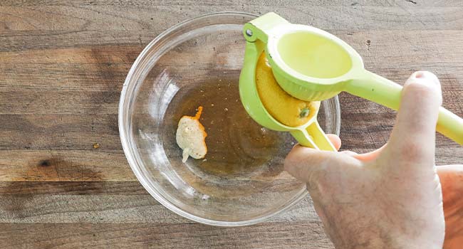 adding lemon juice to a bowl with vinegar and mustard