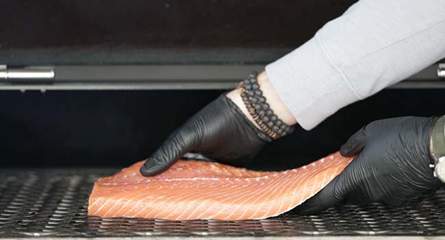 adding a salmon onto a smoker