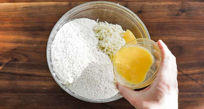 pouring whisked eggs into a bowl of flour and mashed potatoes
