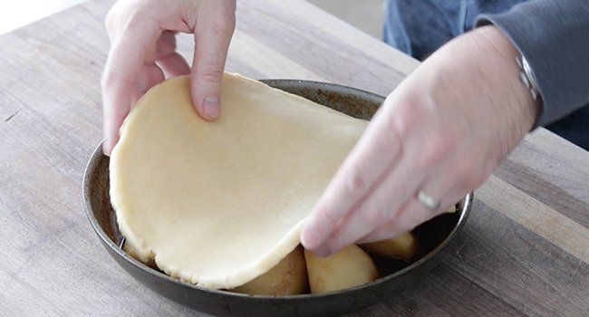 placing dough over cooking apples