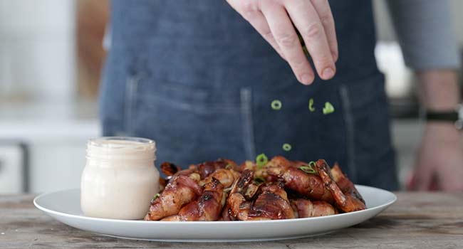 garnishing bacon-wrapped shrimp with green onions