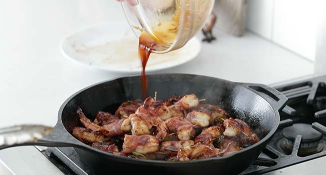 adding soy sauce to cooked bacon-wrapped shrimp