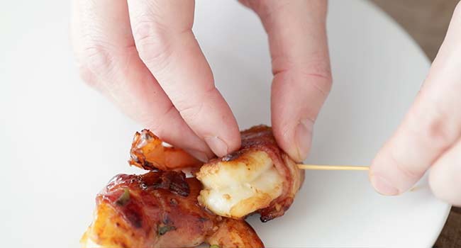 adding bacon-wrapped shrimp to a plate and removing the toothpich
