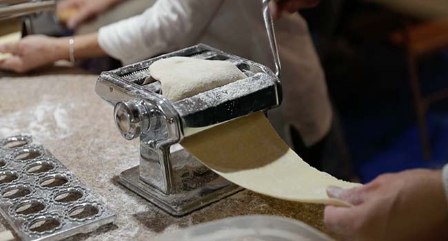 running pasta dough through a pasta maker