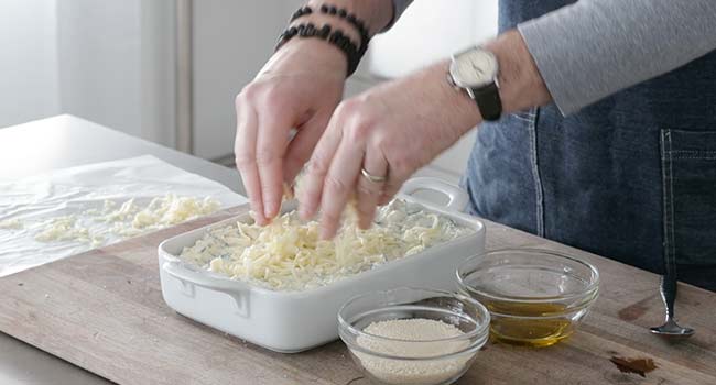 adding cheese to a artichoke and spinach dip