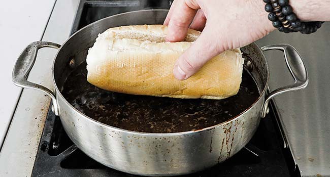 dipping the bottom part of a bun in hot au jus