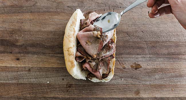 adding hot roast beef to a dipped bun