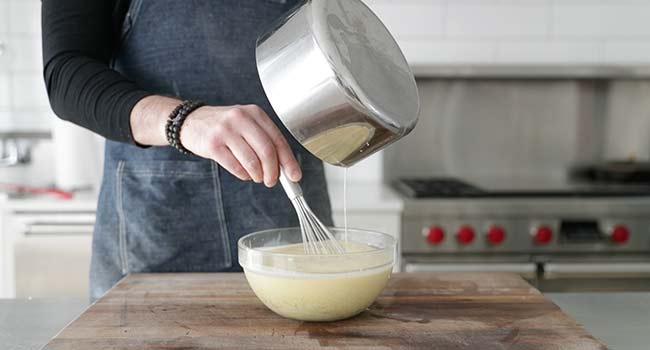 adding hot cream to a bowl of tempered eggs