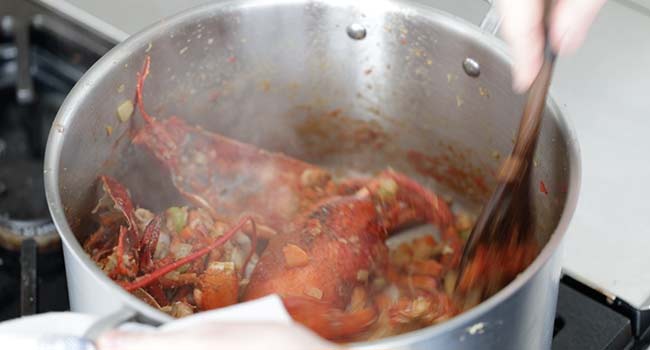 adding tomato paste to a pot with lobsters