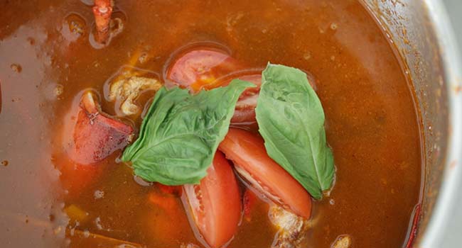 adding tomatoes and basil to a lobster stock