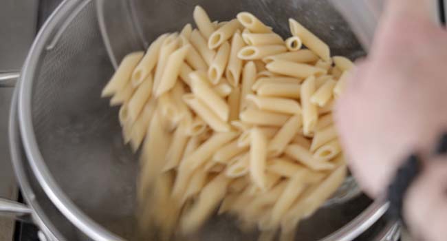 adding penne pasta to a pot of boiling water