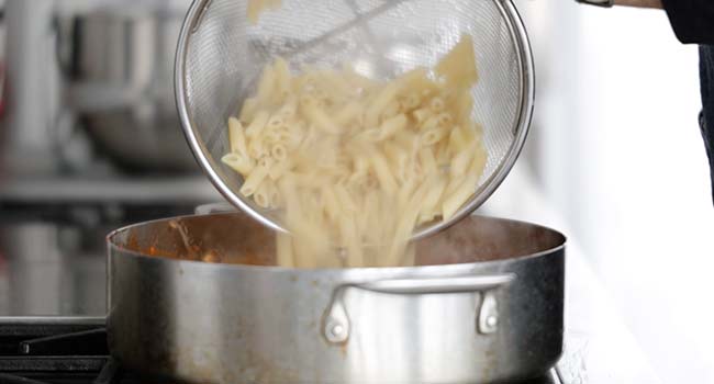 adding cooked penne pasta to a pan