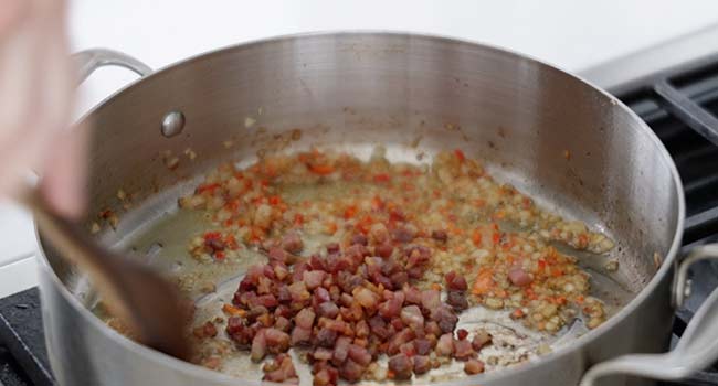 adding cooked pancetta to onions and peppers