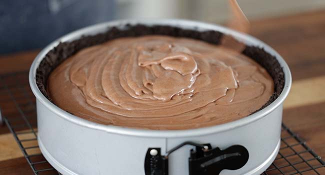 pouring cheesecake batter into a pan with oreo crust