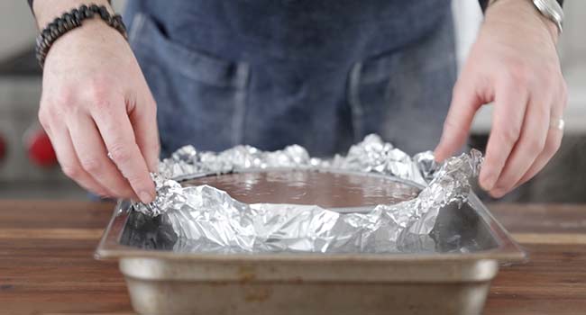 adding a chocolate cheesecake into a hot water bath