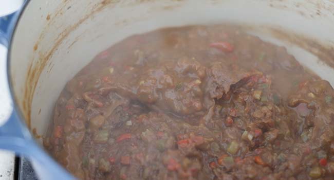 adding stock to a pot of roux and vegetables