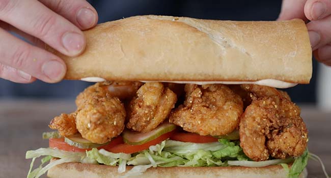 adding the top bun to a po'boy sandwich