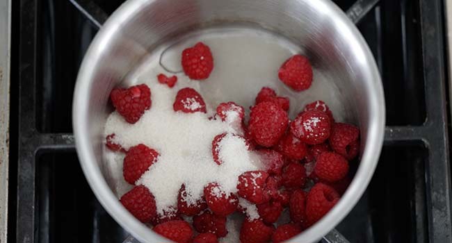 adding raspberries and sugar to a pot