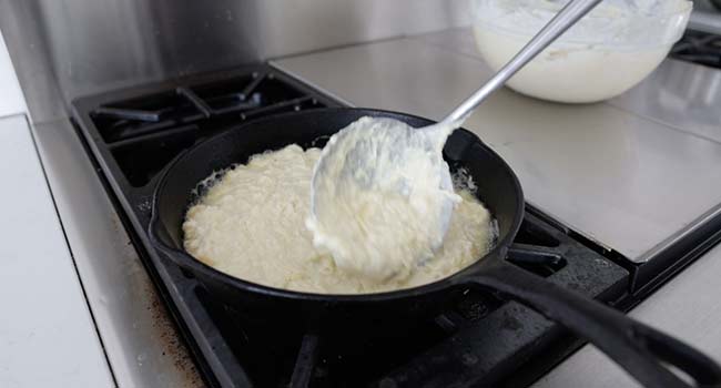 pouring potato pancake batter into a hot cast iron skillet