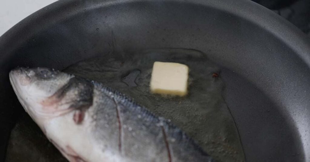 adding butter to a pan with branzino