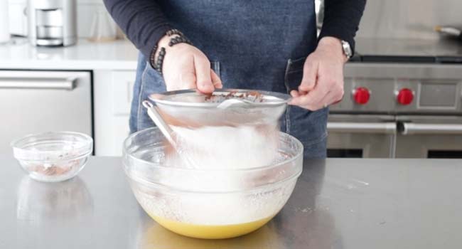 sifting flour and cocoa into a bowl with eggs