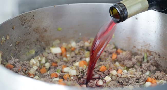 adding wine to a pot with beef and vegetables