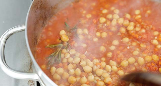 adding chickpeas to a pot with tomatoes