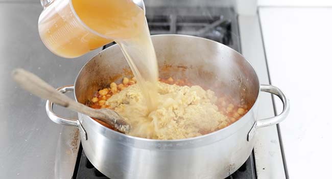 adding chicken stock to a pot of chickpeas and tomatoes