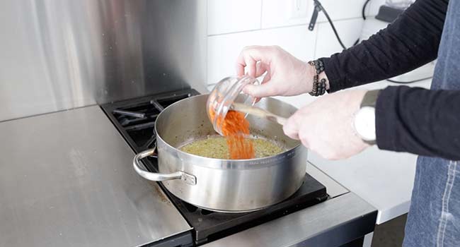 adding carrots to a pan of onions