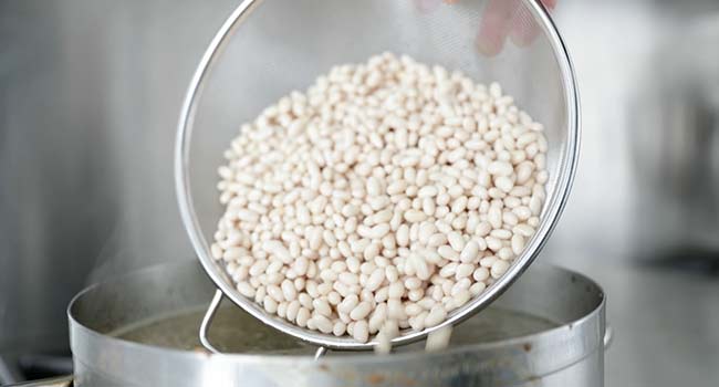 adding soaked beans to a pot