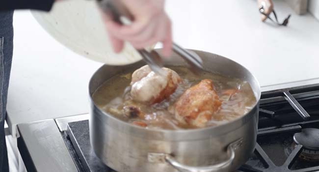 Adding chicken to a pan with seasoned chicken stock