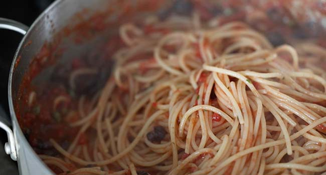 tossing pasta with puttanesca sauce