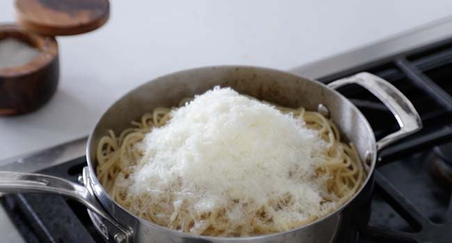 adding pecorino romano into a pot of hot pasta