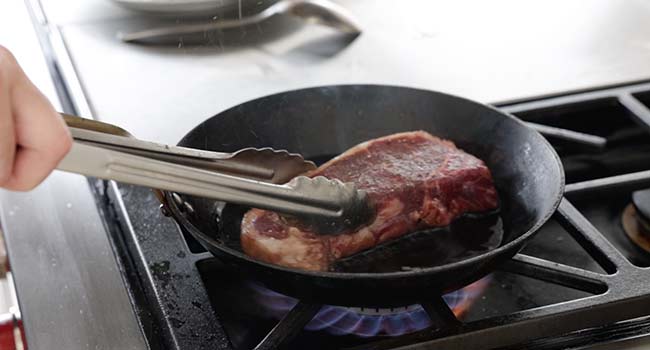 adding a steak to a pan