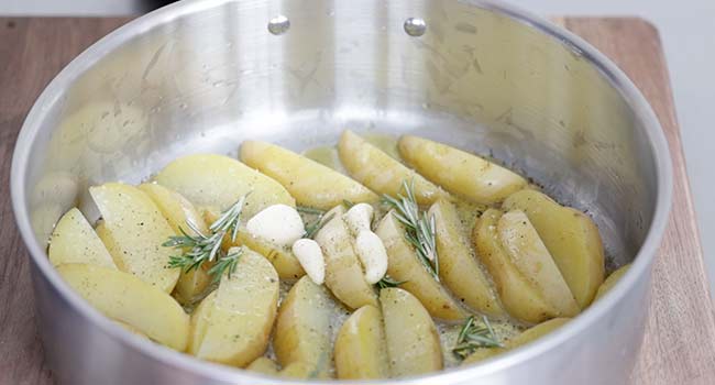 adding rosemary and garlic to potatoes