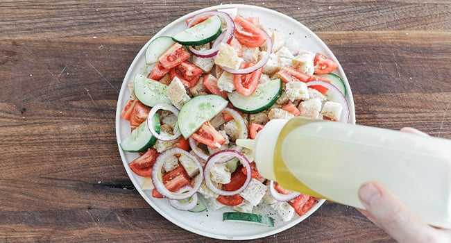 adding vinegar and oil to a panzanella salad