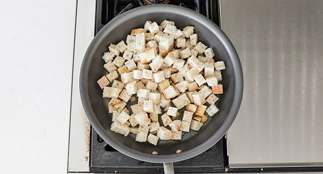 adding cubed bread to a pan of oil