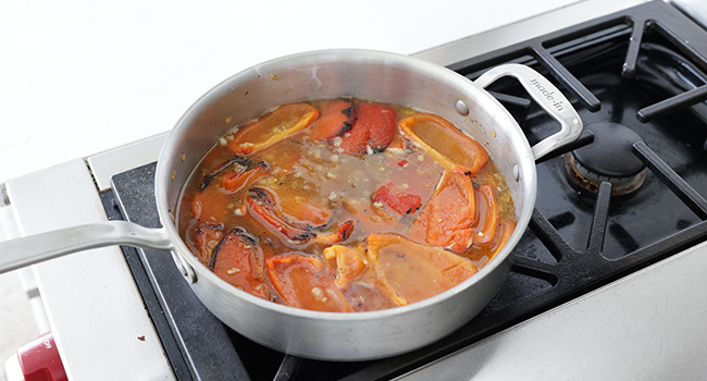 adding chicken stock to a pan of roasted peppers