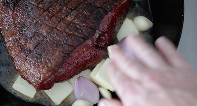 adding butter to a pan with steak