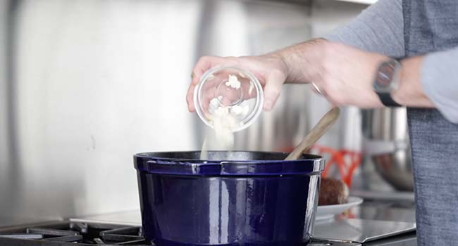 adding garlic to a pot