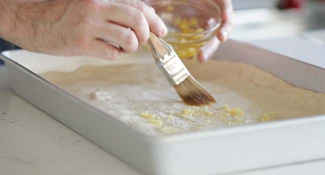 brushing garlic and olive oil onto pizza dough