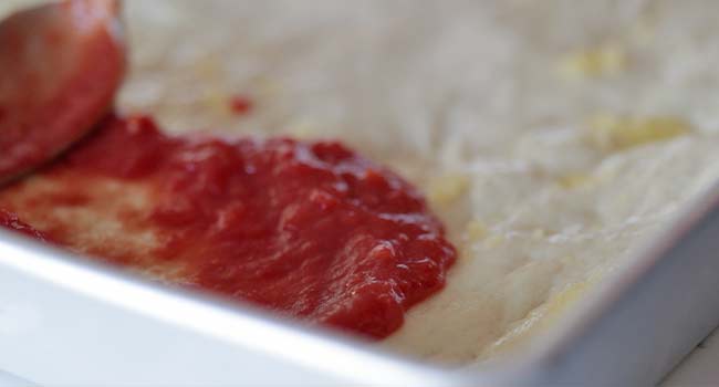 adding tomato sauce to pizza dough