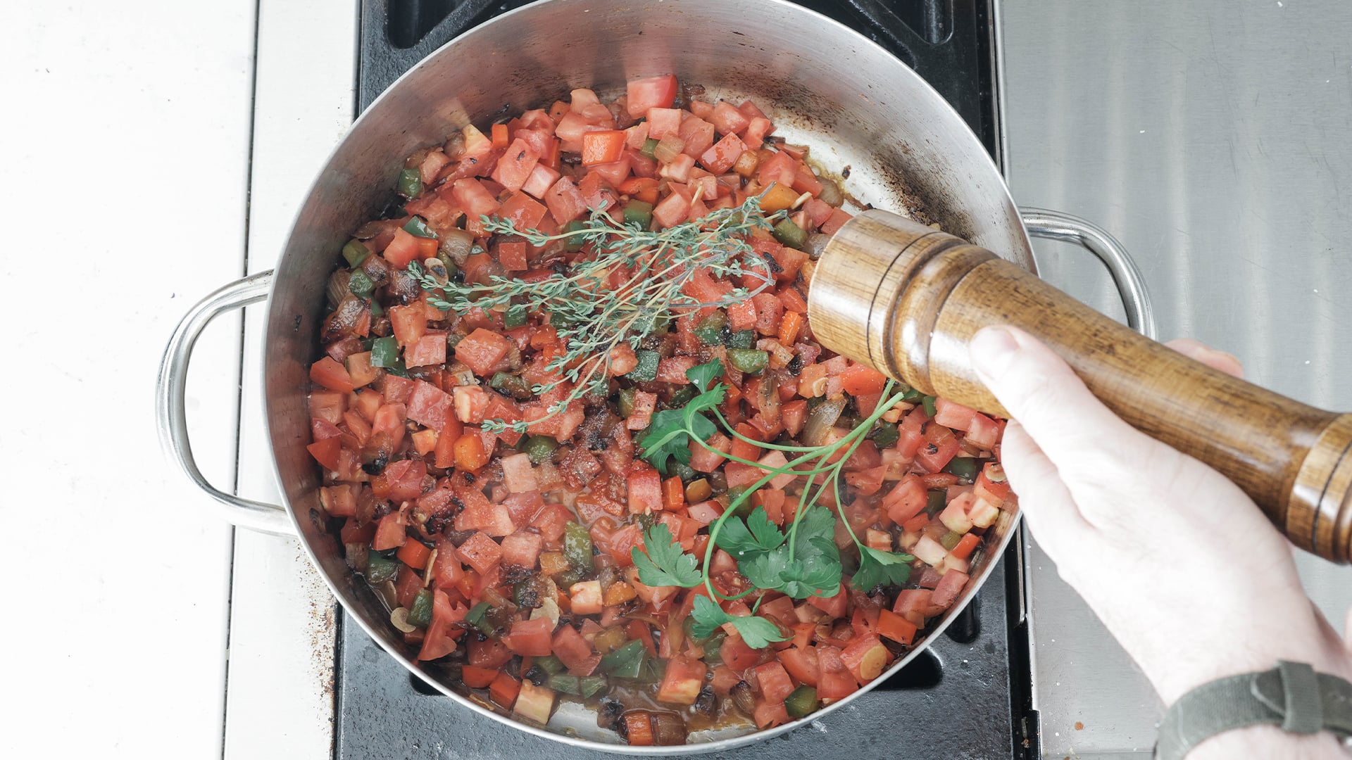 adding pepper to a pot of tomatoes and herbs