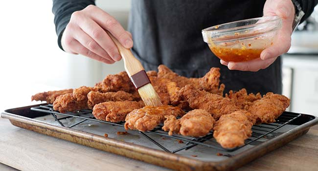 brushing chicken tenders with hot honey sauce