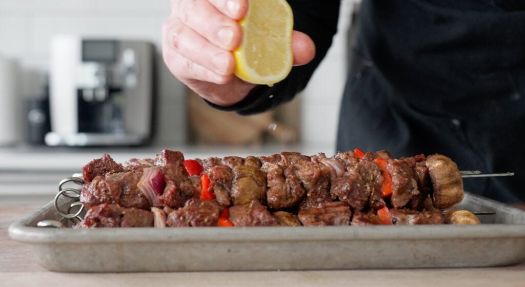 lemon being squeezed over cooked steak kebabs