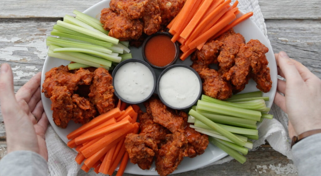 platter of cooked buffalo wings with veggies and sauce