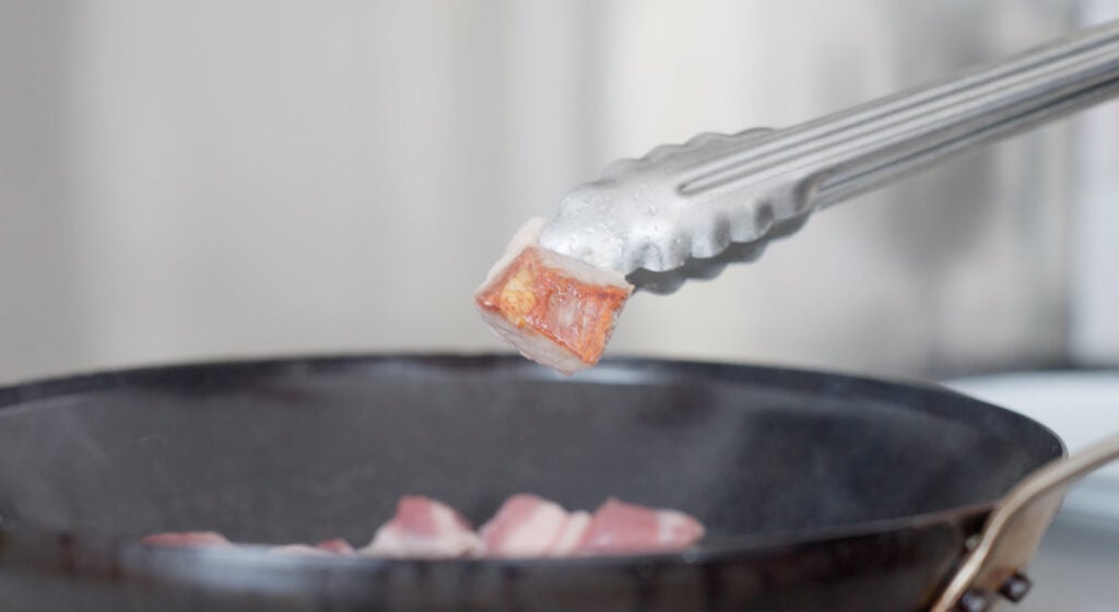 Tongs holding browned piece of pork