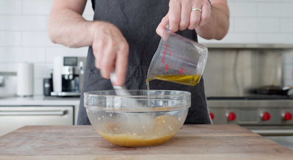 Adding oil into bowl and whisking red wine vinaigrette ingredients