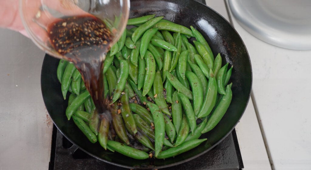 pouring sauce on peas in skillet
